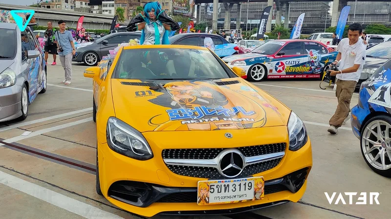 คอสเพลเยอร์ยืนอยู่ในรถเปิดประทุน Mercedes-Benz สีเหลืองลายอิตาฉะตกแต่งกราฟิกอนิเมะในงานรวมพลรถกลางแจ้ง