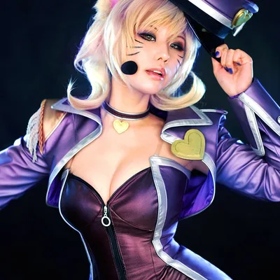 A cosplayer dressed as Popstar Ahri from League of Legends wears a purple outfit, fox ears, and tilts a peaked cap against a dark backdrop.