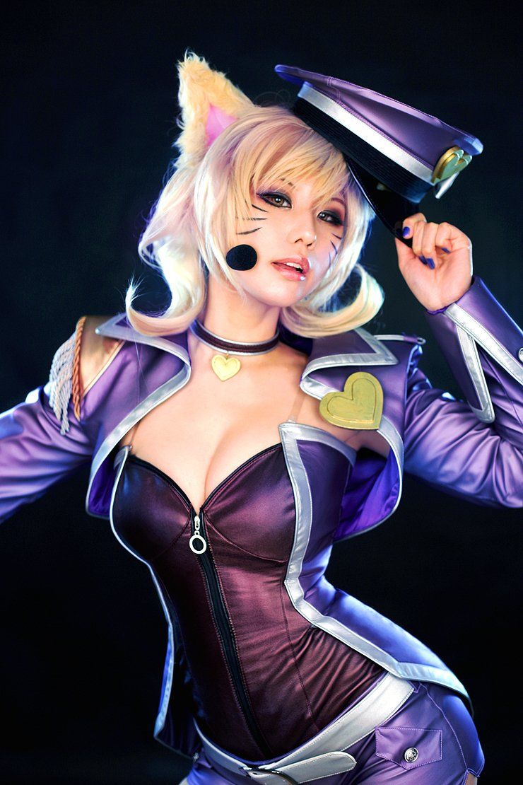 คอสเพลเยอร์ในชุด Popstar Ahri จาก League of Legends สวมชุดสีม่วง ติดหูจิ้งจอก และจับหมวกทรงหม้อตาลบนพื้นหลังสีเข้ม