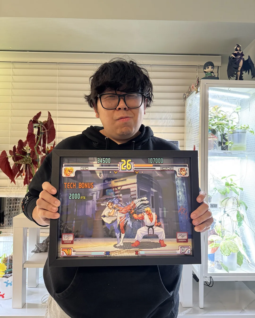 Justin Wong holds a framed 3D shadowbox depicting the famous Evo Moment 37 fight from Street Fighter III: 3rd Strike.