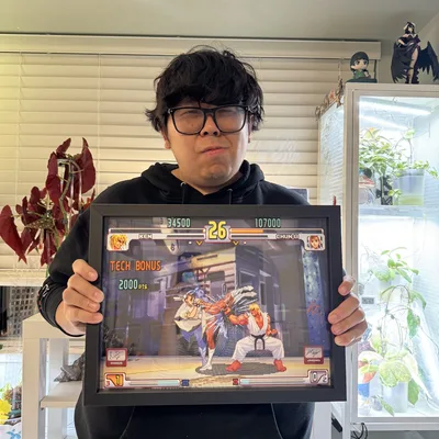 Justin Wong holds a framed 3D shadowbox depicting the famous Evo Moment 37 fight from Street Fighter III: 3rd Strike.