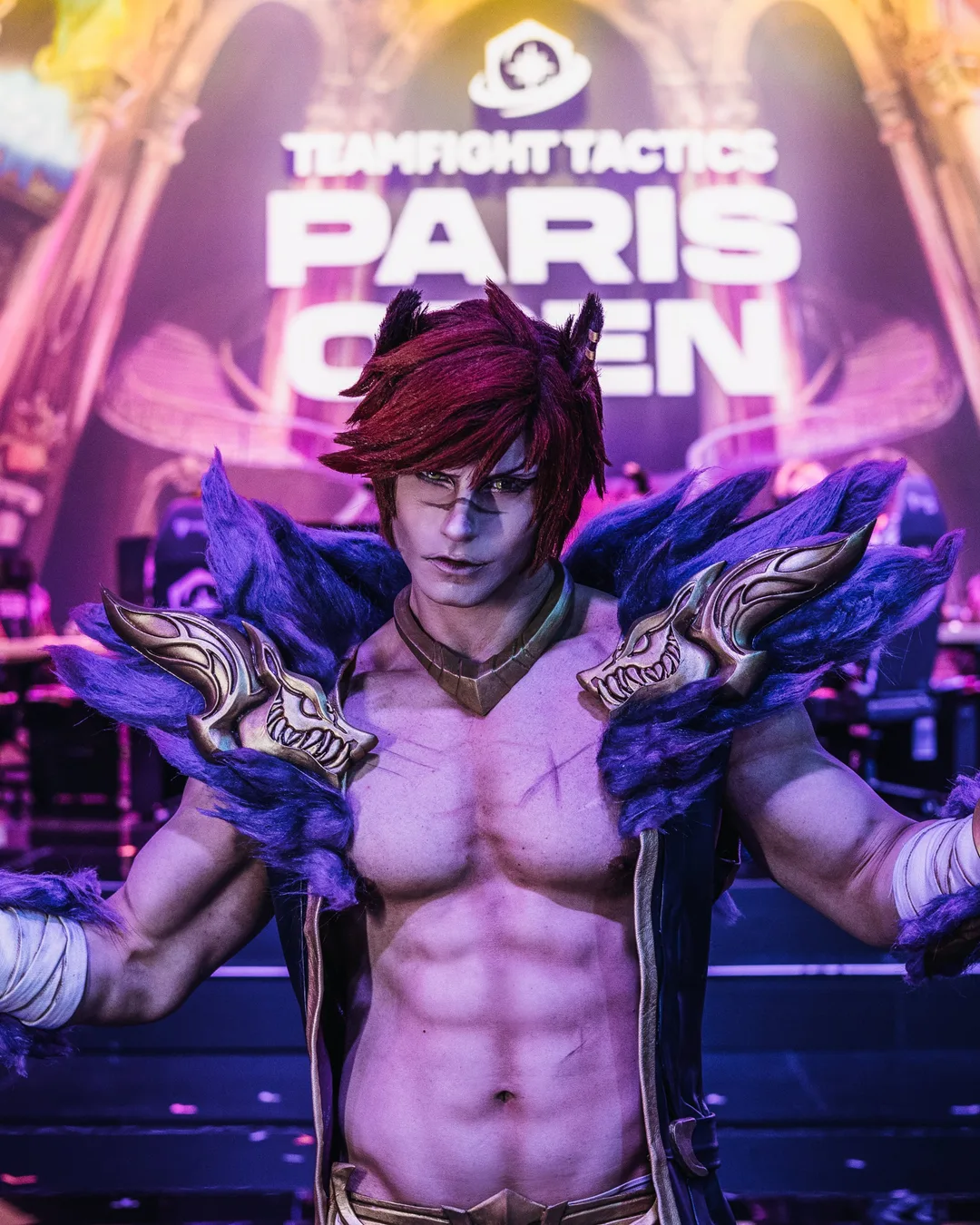 A cosplayer dressed as Sett from League of Legends poses shirtless on a lighted stage at the Teamfight Tactics Paris Open event.