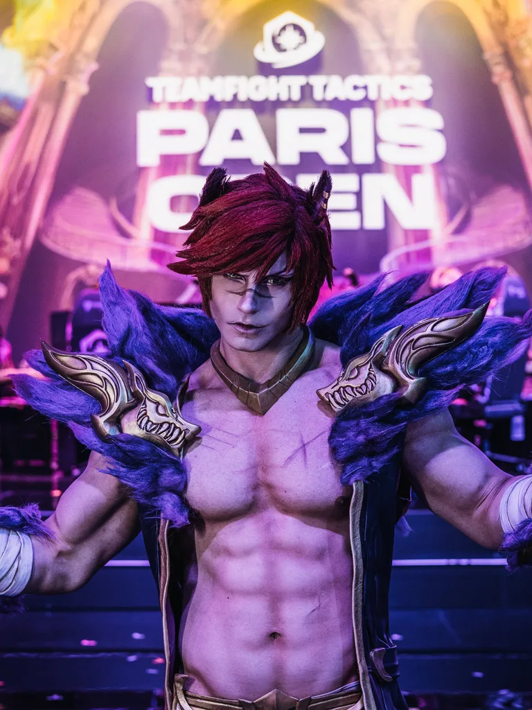 คอสเพลเยอร์ในชุด Sett จาก League of Legends โพสท่าถอดเสื้อบนเวทีที่มีแสงไฟในงาน Teamfight Tactics Paris Open