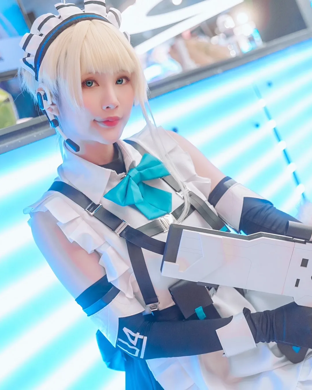 คอสเพลเยอร์ในชุด Toki จาก Blue Archive โพสท่าถือปืนพรอปสไตล์ล้ำยุคหน้าผนังไฟนีออนสีฟ้าในงานอีเวนต์