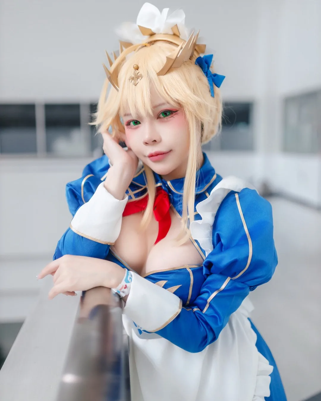 คอสเพลเยอร์ในชุดเมดสีน้ำเงินและขาวสไตล์ Artoria Pendragon เท้าแขนกับราวระเบียงพร้อมมองกล้องในอาคาร