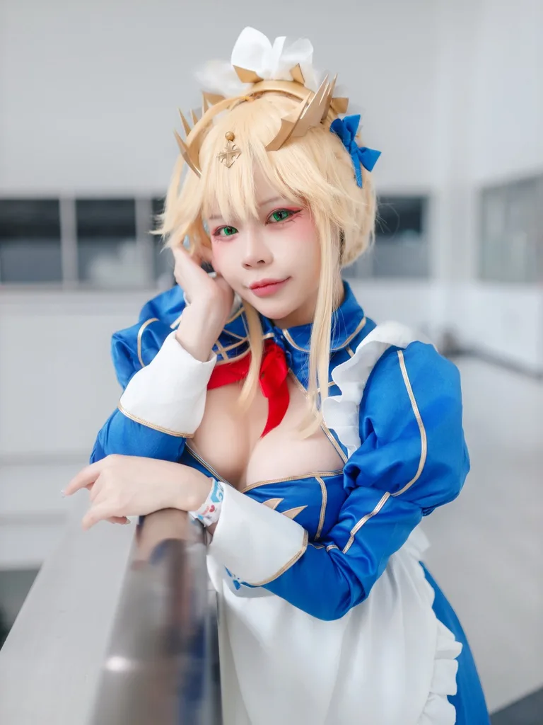 คอสเพลเยอร์ในชุดเมดสีน้ำเงินและขาวสไตล์ Artoria Pendragon เท้าแขนกับราวระเบียงพร้อมมองกล้องในอาคาร