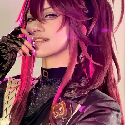A person in cosplay with long magenta hair tied into high pigtails smiles with a gloved hand resting near their chin.
