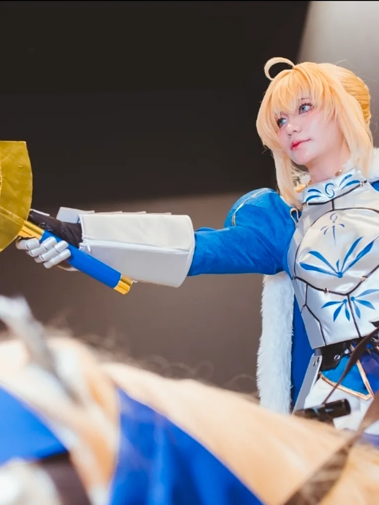 คอสเพลเยอร์แต่งกายเป็น Saber จากซีรีส์ Fate ถือดาบ Excalibur ขณะสวมชุดเกราะอัศวินสีน้ำเงินและสีเงิน