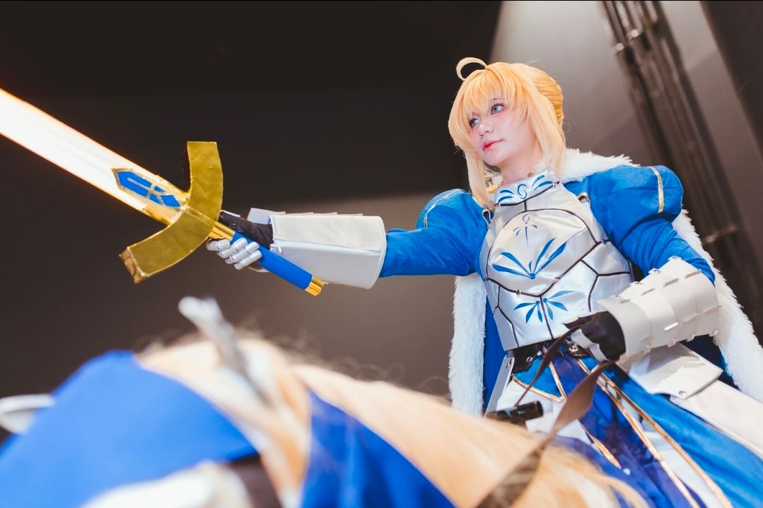 คอสเพลเยอร์แต่งกายเป็น Saber จากซีรีส์ Fate ถือดาบ Excalibur ขณะสวมชุดเกราะอัศวินสีน้ำเงินและสีเงิน