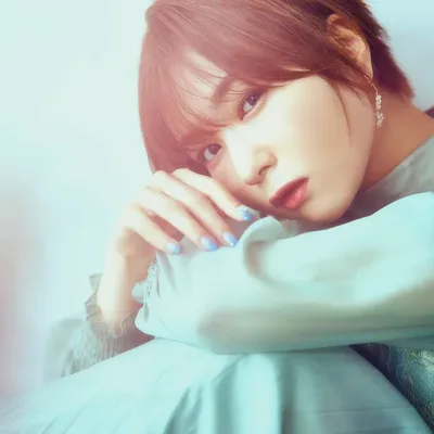 A woman with short reddish-brown hair wearing a mint green blouse rests her chin on her arm and gazes softly at the camera.